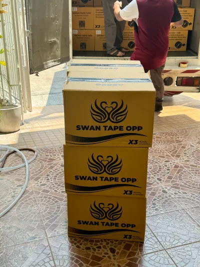ลังเทป OPP ตราหงส์สามใบวางซ้อนกันหน้าท้ายรถบรรทุกระหว่างขนของ — SWAN TAPE โรงงานผลิตเทปกาว