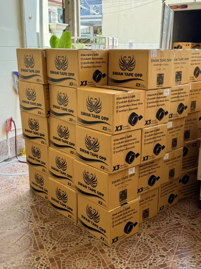 กองลังเทป OPP ตราหงส์เรียงซ้อนสูงรอขนขึ้นตู้รถบรรทุกที่จอดรออยู่ — SWAN TAPE โรงงานผลิตเทปกาว