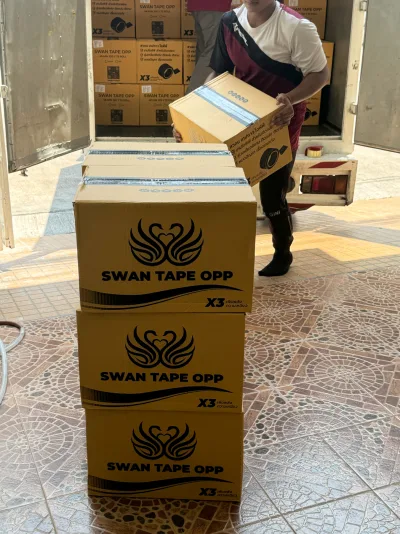 พนักงานยกกล่องเทปลงจากรถ มีกล่อง SWAN TAPE OPP วางซ้อนรออยู่ — SWAN TAPE โรงงานผลิตเทปกาว