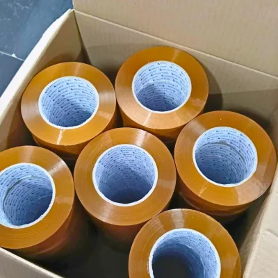 ม้วนเทปสีน้ำตาลเรียงเต็มกล่องกระดาษ ถ่ายจากด้านบนเห็นแกนม้วนสีฟ้า — SWAN TAPE โรงงานผลิตเทปกาว