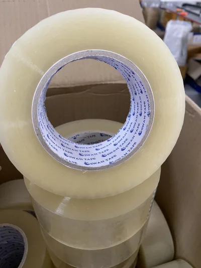 ม้วนเทปใสตั้งอยู่บนกองม้วนเทปในกล่องกระดาษ — SWAN TAPE โรงงานผลิตเทปกาว