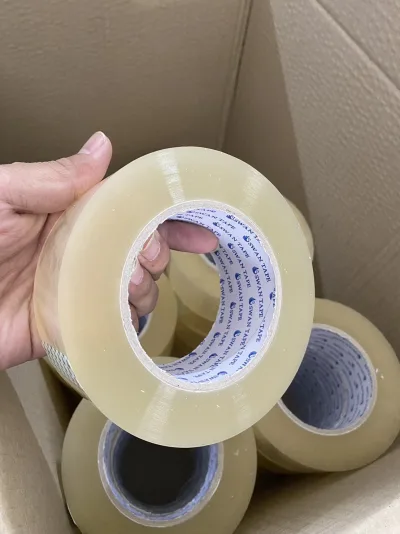 มือพนักงานหยิบม้วนเทปใสขึ้นจากกล่องที่บรรจุม้วนเทป — SWAN TAPE โรงงานผลิตเทปกาว
