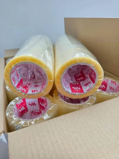 ม้วนเทปใสห่อพลาสติกวางเรียงอยู่ในกล่องลูกฟูกที่เปิดฝา แกนม้วนพิมพ์โลโก้ WS — SWAN TAPE โรงงานผลิตเทปกาว