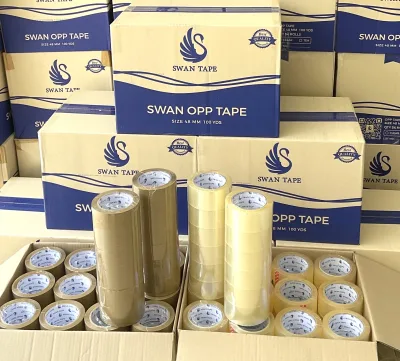 กล่อง SWAN OPP TAPE ซ้อนเป็นกำแพง ด้านหน้าวางม้วนเทปใสและเทปสีน้ำตาลเทียบกัน — SWAN TAPE โรงงานผลิตเทปกาว