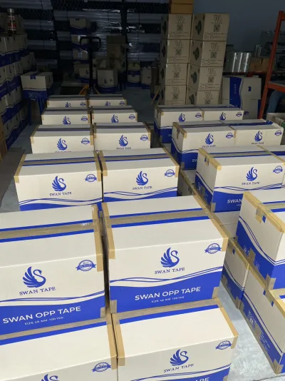 ลังเทปกาว SWAN OPP TAPE ขนาด 48 มม. 100 หลา วางเรียงเต็มพื้นคลัง มีรถลากพาเลทจอดอยู่ — SWAN TAPE โรงงานผลิตเทปกาว